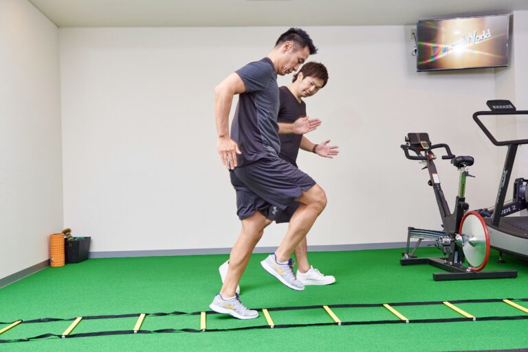 ラダーを使った動きのトレーニングを、手振りを交えて説明するトレーナー
