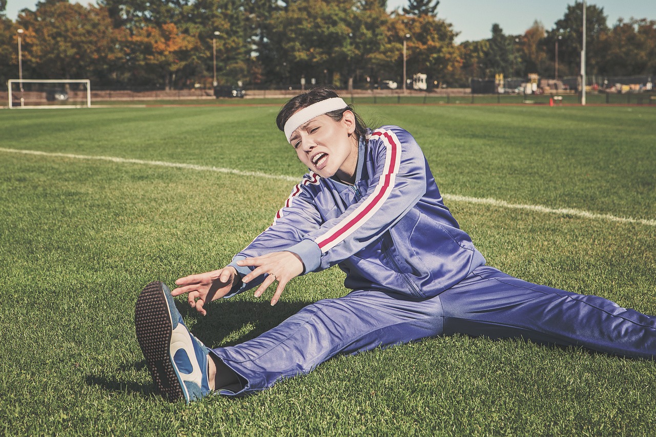 昼休みの運動は30分で意味がある?短い運動の効果と汗・食事の組み方 1 芝生のグラウンドで開脚ストレッチをするジャージ姿の男性。短い時間でも身体は動かせる