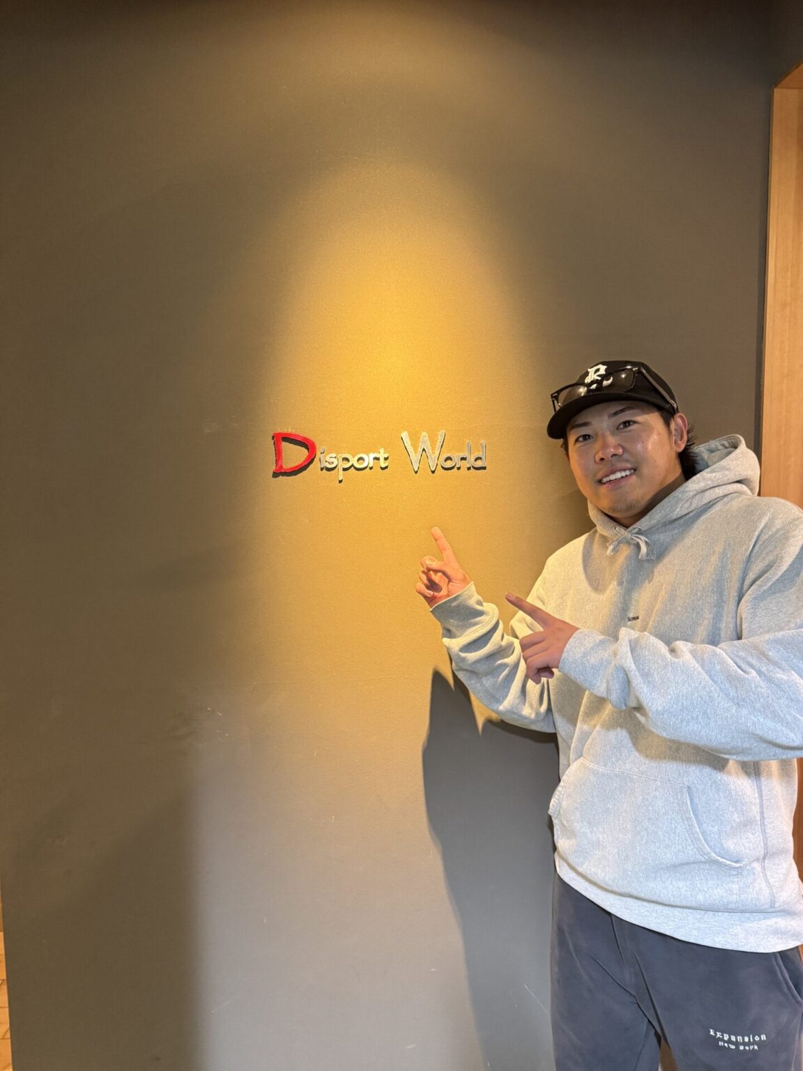 赤羽由紘選手が六本木の店舗でDisport Worldの壁ロゴを指差している