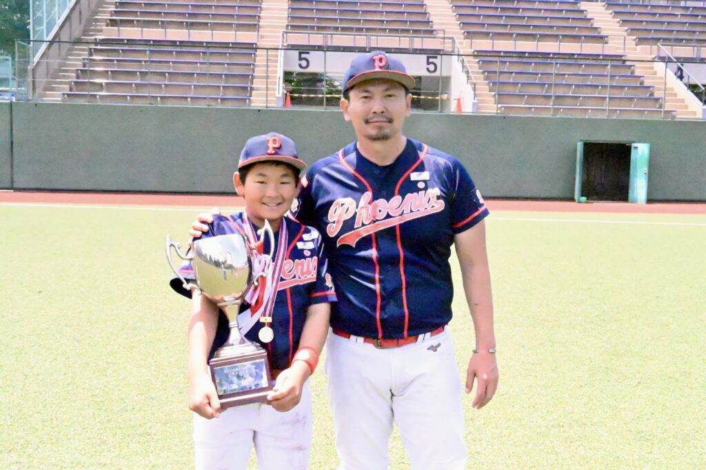 船橋フェニックスのユニフォームを着て、トロフィーとメダルを手にした子どもと並ぶ監督の岡本隼人